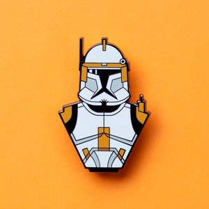 May include: A white and orange enamel pin of a Star Wars clone trooper with a black visor and a white background.