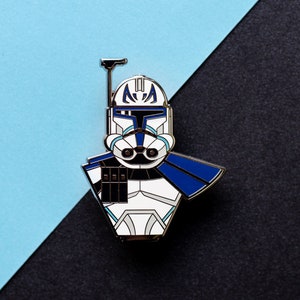 Peut inclure: Épingle en émail représentant un soldat clone de Star Wars. L'épingle a une base blanche avec des détails bleus et noirs, et un contour en métal argenté. Le fond est divisé en diagonale, avec des sections bleu clair et noir.