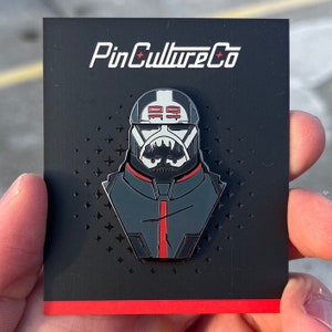 Puede incluir: Pin de esmalte negro y rojo con un personaje de Star Wars con casco y una raya roja en la parte delantera. El pin dice "PinCultureCo" en la parte superior.