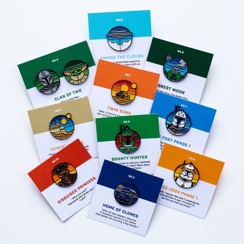 May include: A collection of ten enamel pins featuring characters and scenes from Star Wars. The pins are colorful and feature a variety of designs, including the Death Star, a bounty hunter, and a group of clones. Each pin has a number and a quote from the Star Wars universe.