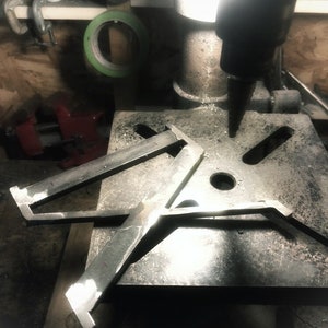 Op de afbeelding: Een metalen boormachine met een zwarte basis en een zilveren boor. Een metalen beugel is op de tafel van de boormachine geplaatst.
