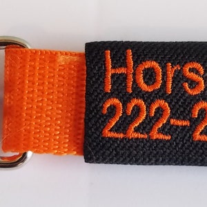 May include: Black and orange horse ID tag with a silver clip. The tag has the text "Horse Name 222-222-2222" embroidered on it.