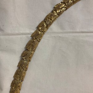 May include: A gold-colored metal decorative trim with a leaf design. The trim is curved and has a ribbon at the top.