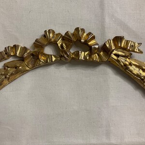 May include: A gold-colored metal frame with a decorative ribbon design. The frame is curved and has a floral pattern.
