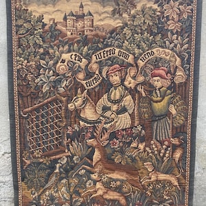 May include: A woven wall tapestry featuring a medieval hunting scene with a person on horseback, a figure on foot, a deer, and hunting dogs. The background displays a castle and forest, with a banner containing the text "C'est ufred oum uend".
