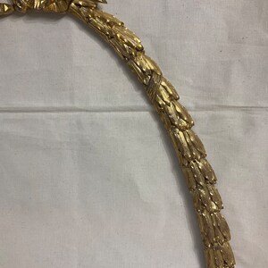 May include: A gold-colored metal decorative piece shaped like a curved wreath with a ribbon at the top.