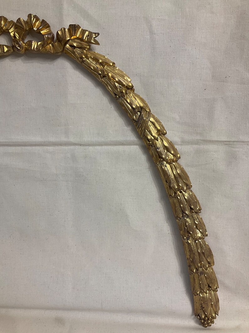 May include: A gold-colored metal decorative piece shaped like a curved wreath with a ribbon at the top.