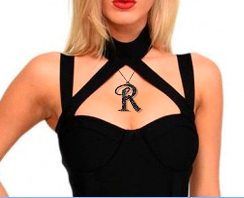 K&ouml;nnte beinhalten: Eine schwarze Choker-Kette mit einem gro&szlig;en, schwarzen, mit Strasssteinen besetzten Anh&auml;nger in Form des Buchstabens "R".