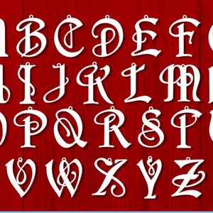 K&ouml;nnte beinhalten: Wei&szlig;e, dekorative, kursive Buchstaben des Alphabets mit einem Loch oben zum Aufh&auml;ngen. Die Buchstaben befinden sich auf einem roten Holzgrund.