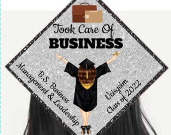 May include: A silver glitter graduation cap with a black and gold graduate figure, the text "Took Care Of BUSINESS", "B.S. Business Management & Leadership", "Veisgeim Class of 2022", and a brown briefcase.
