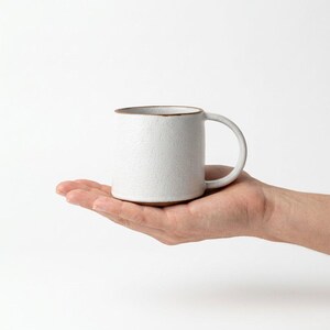 May include: A set of three ceramic mugs with a speckled, matte finish. The mugs are in shades of cream, light gray, and dark gray. Each mug has a simple, minimalist design and a rounded handle.