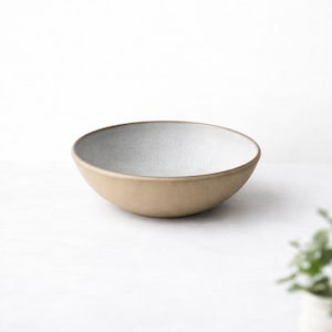 Könnte beinhalten: Eine Keramikschale mit hellbrauner Außenseite und gesprenkelter weißer Innenseite. Die Schale hat ein schlichtes, modernes Design und eignet sich zum Servieren von Speisen. Der Rand ist dunkler braun und setzt einen dezenten Kontrast.