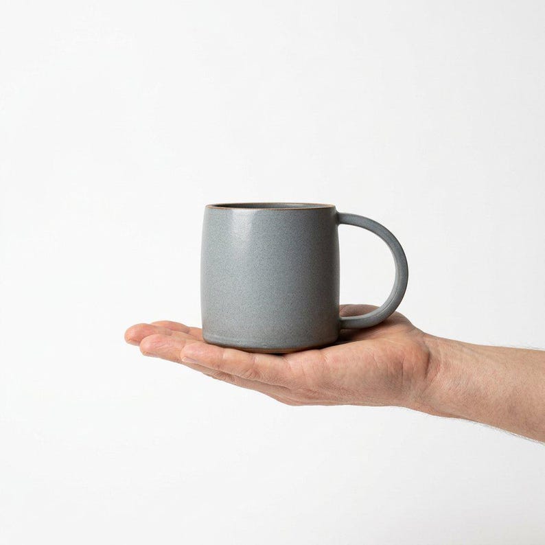 May include: A set of three ceramic mugs with a speckled, matte finish. The mugs are in shades of cream, light gray, and dark gray. Each mug has a simple, minimalist design, perfect for coffee or tea.