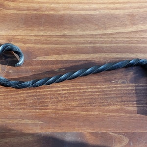 May include: A black metal twisted hook with a 90-degree bend at the end. The hook is designed for hanging items on a wall.