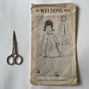 May include: Vintage sewing pattern for a child's dress. The pattern is for a 6-year-old and has a 25-inch chest measurement. The pattern is from Weldons and has the number 8032.