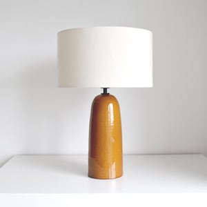 May include: A ceramic table lamp with a mustard yellow base and a white drum shade.