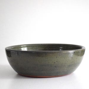 Puede incluir: Un cuenco de cer&aacute;mica hecho a mano con un esmalte verde oscuro. El cuenco tiene una forma redondeada con un borde ligeramente ensanchado y una base marr&oacute;n rojiza. El cuenco es adecuado para servir alimentos.