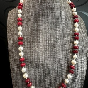 Peut inclure: Un long collier composé d'une alternance de perles blanches rondes et de perles en pierre précieuse rouge foncé à facettes. De petites perles intercalaires en métal argenté sont placées entre chaque perle pour un design uniforme.