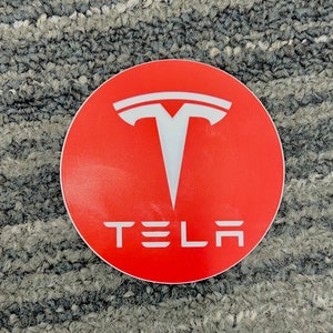 May include: A red circle sticker with a white Tesla logo and the word "TESLA" in white letters.