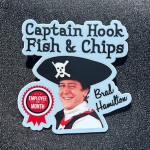 May include: A blue and white sticker with the text "Captain Hook Fish & Chips" and a picture of a man dressed as Captain Hook. The man is smiling and has a red "Employee of the Month" badge. The text "Brad Hamilton" is written below the picture.