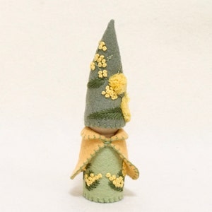 May include: A felt gnome doll with a green pointed hat embroidered with yellow flowers and leaves. The gnome is wearing a yellow cape and has a green felt body.