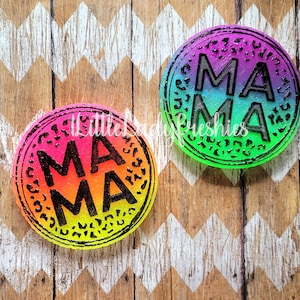 May include: Two round, colorful coasters with a black outline and the word "MAMA" written in black letters. The coasters have a rainbow gradient design.