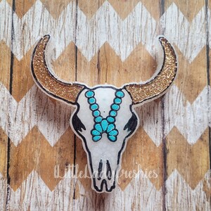 May include: A white glitter bull skull with gold glitter horns and a turquoise beaded necklace.