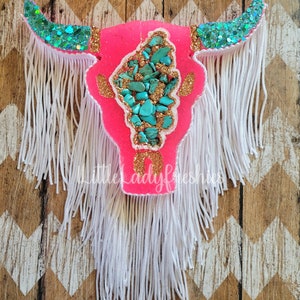 May include: Pink and turquoise cow skull with gold glitter and white fringe.