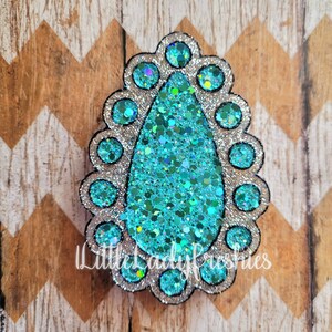 May include: A teal blue glitter teardrop shape with a silver glitter border and a silver glitter outline. The teardrop is surrounded by a silver glitter circle with a black outline. The teardrop is on a brown and white chevron background.
