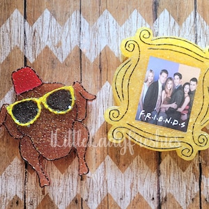 Puede incluir: Un marco amarillo con la palabra "FRIENDS" impresa en &eacute;l. El marco tiene una foto de seis personas dentro. Un pavo de dibujos animados marr&oacute;n que lleva un fez rojo y gafas de sol est&aacute; al lado del marco.