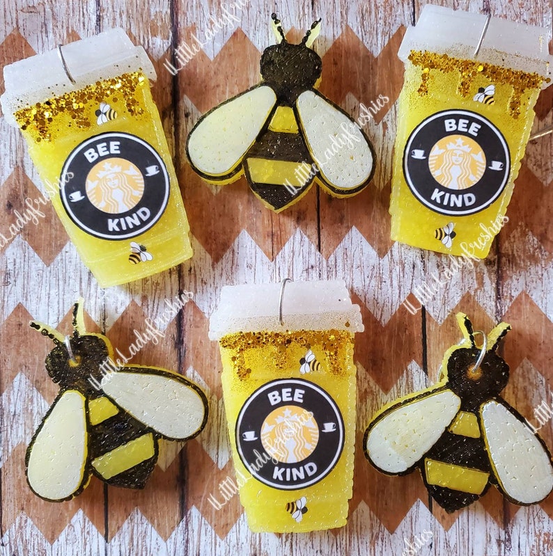 K&ouml;nnte beinhalten: Vier gelbe und wei&szlig;e bienenf&ouml;rmige Auto-Lufterfrischer. Zwei sind in Form von Kaffeetassen mit der Aufschrift "Bee Kind". Die anderen beiden sind bienenf&ouml;rmig mit schwarzen und gelben Streifen.
