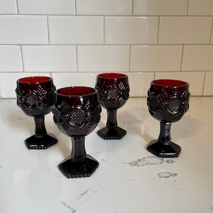 May include: Four dark red glass wine goblets with a textured design. The goblets have a round bowl and a stem with a hexagonal base.