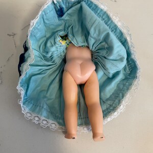 May include: A vintage doll with a blue and white dress and lace trim. The doll is missing its head and arms.