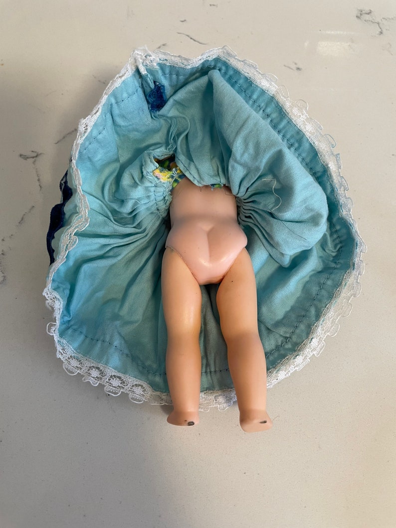 May include: A vintage doll with a blue and white dress and lace trim. The doll is missing its head and arms.