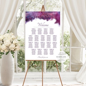 May include: Purple and blue watercolor wedding seating chart with the word "Welcome" at the top. The chart lists table numbers and guest names. The chart is displayed on an easel.
