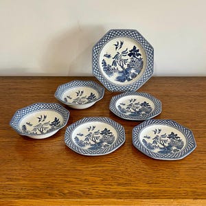May include: A collection of six blue and white ceramic dishes. The set comprises a large octagonal plate and five smaller, oval-shaped plates. Each item displays a detailed landscape design and a patterned border.