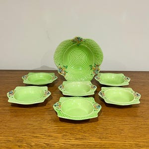 May include: A set of seven green ceramic bowls with floral designs. The bowls are arranged in a circle with a larger bowl in the center.