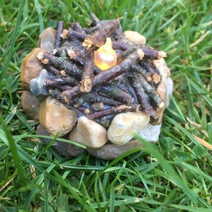 May include: A miniature campfire made of small twigs and stones with a glowing light in the center.