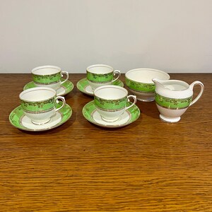 May include: A set of green and white teacups and saucers with a gold trim. The set includes a creamer and a sugar bowl.