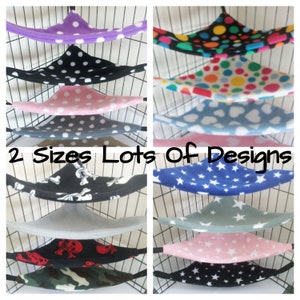 Puede incluir: Una colección de hamacas de tela coloridas y estampadas para mascotas pequeñas. Las hamacas son de varios colores y patrones, incluyendo lunares, estrellas, corazones y calaveras. El texto "2 Sizes Lots Of Designs" es visible en la imagen.