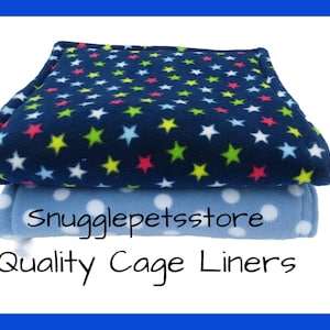 Può includere: Due fodere per gabbia impilate. La fodera superiore è blu navy con motivi a stelle colorate. La fodera inferiore è azzurra con pois bianchi. Il testo "Quality Cage Liners" è visibile.