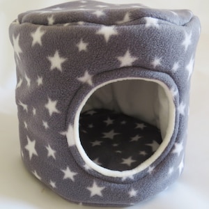 May include: A gray and white star patterned fleece pet bed with a round opening. The bed is designed for small animals like hamsters or gerbils.