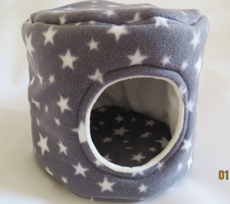 May include: A gray and white star patterned fleece pet bed with a round opening. The bed is designed for small animals like hamsters or gerbils.