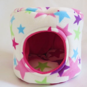 May include: A white fleece pet bed with a pink interior and a star pattern in pink, blue, green, and purple.