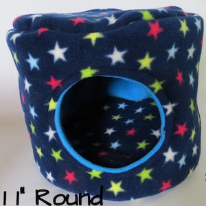 May include: A blue fleece pet bed with a round opening. The bed is covered in a pattern of white, pink, yellow, and light blue stars. The bed is 11 inches in diameter.