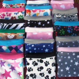 Op de afbeelding: Een verzameling kleine huisdierbedden gemaakt van fleece. De bedden hebben verschillende patronen, waaronder pootafdrukken, sterren en dierenontwerpen. Elk bed heeft een contrasterende rand in kleuren als blauw, roze en grijs. De bedden zijn ontworpen voor kleine huisdieren.