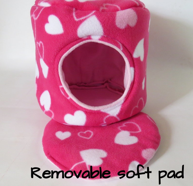 May include: Pink and white heart patterned fleece pet bed with a removable soft pad. The bed has a round opening for the pet to enter.