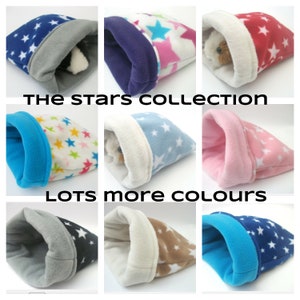 Puede incluir: Una colección de nueve camas acogedoras para mascotas de forro polar con un patrón de estrellas. Las camas son de varios colores, incluidos azul, rosa, rojo, marrón y gris. El texto "THE STARS COLLECTION" y "LOTS MORE COLOURS" se muestra en la imagen.