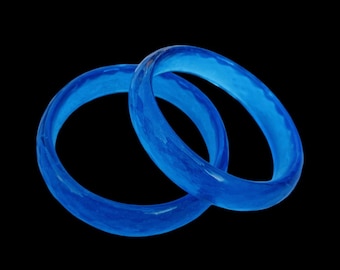 May include: Two blue glass rings, one slightly larger than the other, are stacked on top of each other. The rings are translucent and have a slightly rippled texture.