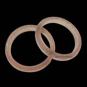 May include: Two translucent pink glass bangles with a subtle shimmer. The bangles are stacked on top of each other.